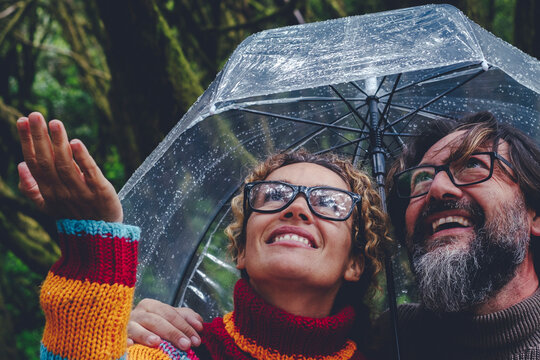 One couple have fun and enjoy bad weather rain under a transparent umbrella smiling together and checking drops water. Outdoor leisure activity in winter season for man and woman in friendship