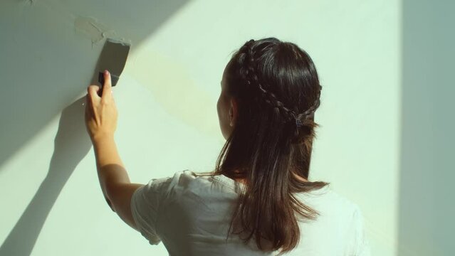 Woman applying plaster on wall. DIY house renovation, female worker rear view. Putty of joints on finishing works, home interior design concept, slow motion