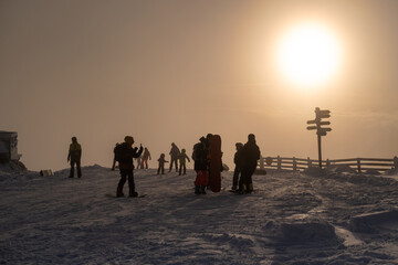 Silhouettes of resting snowboarders and skiers in the ski resort at sunset on the top of the mountain