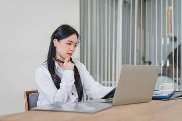 Smiling millennial Asian female office worker working with financial reports for tax audit reports or financial statement in a meeting room.