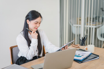 Smiling millennial Asian female office worker working with financial reports for tax audit reports or financial statement in a meeting room.
