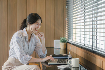 Smiling young asian businesswoman using laptop to work online, remote work.