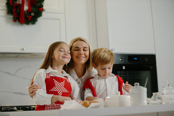 Two happy children hug their mother while making Christmas cookies at home during winter holidays. Happy mother having fun with her children in the kitchen at home.