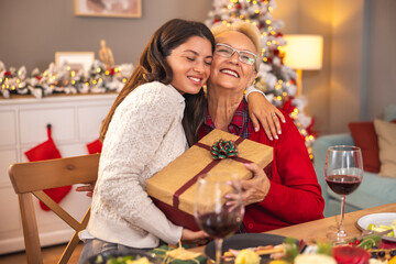 Mother and daughter exchanging presents while having Christmas dinner at home