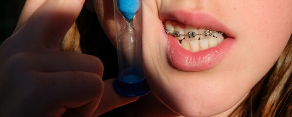 A child's mouth with braces on the upper teeth. A clepsydra in a girl's hand. Daily dental care.