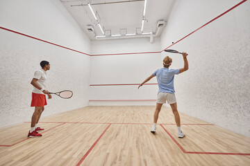 active and interracial friends playing squash together inside of court, preparing for competition