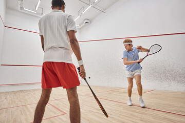 active multiethnic men in sportswear playing squash inside of court, challenge and motivation