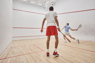 interracial active men in sportswear playing squash inside of court, challenge and motivation