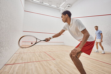 young and active multicultural men playing squash inside of court, challenge and motivation