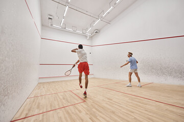 interracial players in sportswear playing squash together inside of court, fitness and motivation