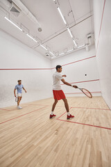 Fototapeta premium young interracial sportsmen playing squash together inside of indoor court, motivation and sport