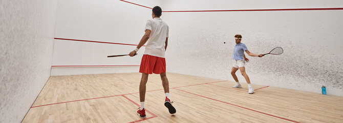 Fototapeta premium interracial athletic men in sportswear playing squash together inside of court, motivation banner