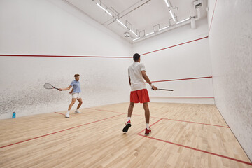 interracial and athletic men in sportswear playing squash together inside of court, motivation