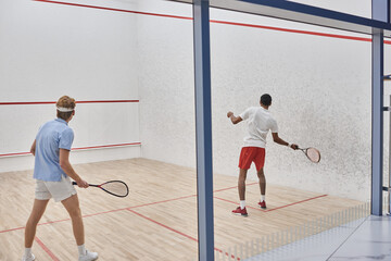 multicultural players in sportswear playing squash together inside of court, motivation and sport