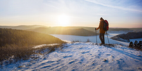 Man with backpack walking up a hill at sunset.  Winter hiking. Banner with copy space.