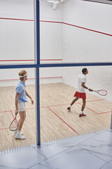 multicultural friends in sportswear playing squash together inside of court, motivation and sport