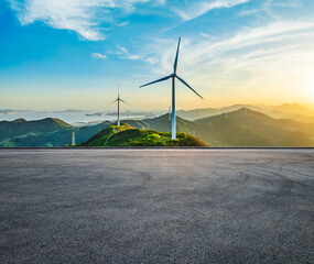 Asphalt road and wind turbines with mountain natural landscape at sunset. High Angle view.