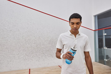 athletic african american sportsman in active wear holding bottle of water after playing squash