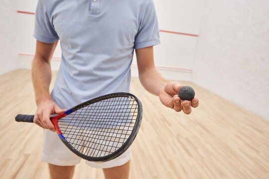 cropped view of man in sportswear holding squash ball and racquet and standing inside of court