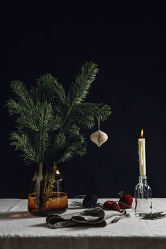 winter holidays and celebration concept - close up of fir branch in vase with christmas toys and candle burning on table over black background