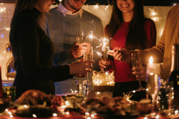 Night shot of people toasting with champagne and holding sparklers while having New Year 