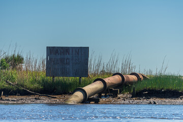 A faded sign next to a pipeline entering the Cape Fear River from the shore, near Wilmington, North Carolina