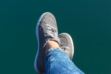 Woman's feet in canvas sneakers above blue water surface background. Summer vibes. Relaxation...