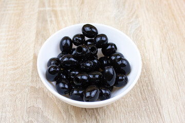 Pitted black olives in a white cup on the table. Canned olives, recipe, food.