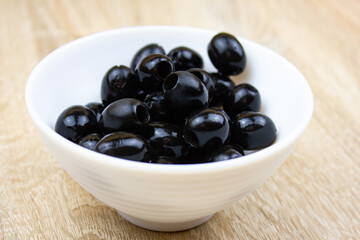 Pitted black olives in a white cup on the table. Canned olives, recipe, food.