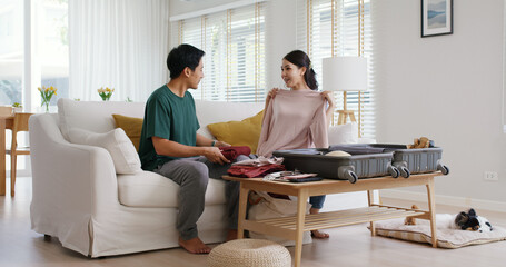 Fototapeta premium Relax safe get away ready to get back to road trip. Asia people man woman choose clothing with love smile happy plan enjoy dating sit laugh fun folding stuff stack face mask open and neat bag at home.