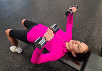Overhead view of female athlete doing bench press workout with dumbbell in fitness room