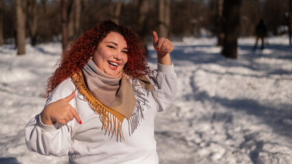 A chubby red-haired woman in a white sweatshirt. Girl fooling around in the park in winter. 