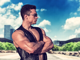 A shirtless muscular man standing on the side of a road, wearing a leather vest on naked muscle...