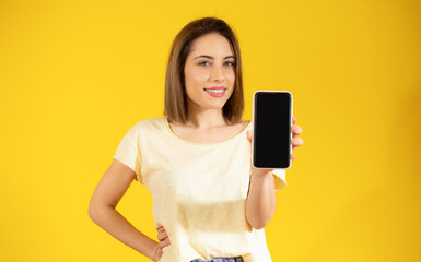 Image of pretty young woman isolated over yellow background. Looking camera showing display of mobile phone.