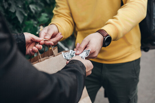 Man pays for food delivery close up .Male courier food delivery man in positive in uniform hands over food order and receives money tips payment from man client in jacket. concept food delivery cash