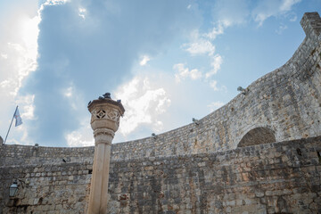Pigeons perched on very old medieval style pillar in Dubrovnik against cloudy sky