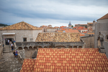 View to the red roofs of Dubrovnik Old town on cloudy summer day. Tourists walking on the walls of city
