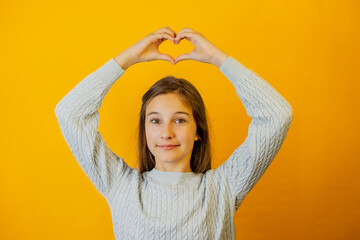 Portrait of small attractive smiling girl she holds her hands above her head and shows heart with her hands