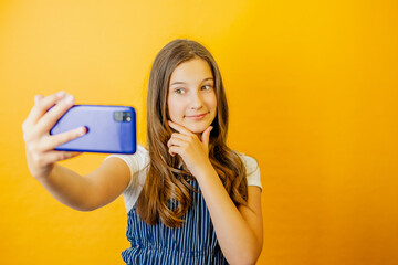 Naklejka premium A charming schoolgirl in a fashionable outfit streams, shows, selfies, blogs on her phone, smiling and cheerful