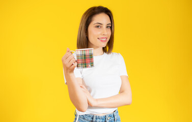 Beautiful young casual woman holding in hand cup of tea over yellow background.