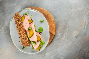 Delicious baguette sandwich with ham and pickled cucumbers on a wooden board. top view. copy space for text