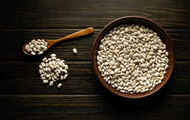 A plate of raw beans and sprinkles near a spoon on an antique table before cooking. Place for recipe or menu on black background