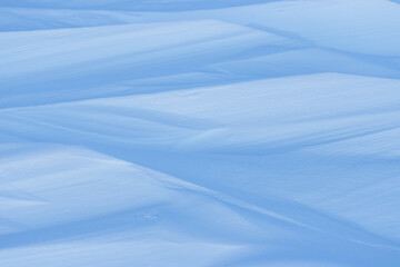 Beautiful winter background with snowy ground. Natural snow texture. Wind sculpted patterns on snow surface.