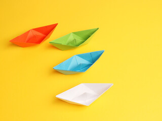 Four different paper boats on a yellow background, teamwork or togetherness concept