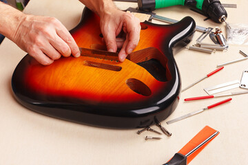 Guitar repairer measures size of holes for tremolo in body of guitar with ruler.