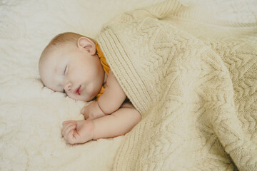 A little boy sleeps under a knitted baby blanket. Portrait of a sleeping baby.