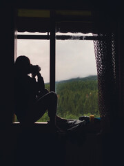 woman near window looking at rainy mountains