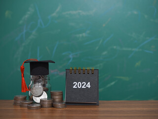 Study goals, 2024 Desk calendar, Glass bottle with graduation hat and stack of coins. The concept of saving money for education, student loan, scholarship, tuition fees in New Year 2024