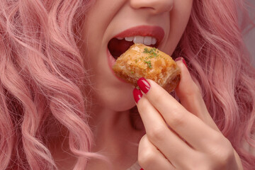 Woman with pink curly hair is eating baklava.