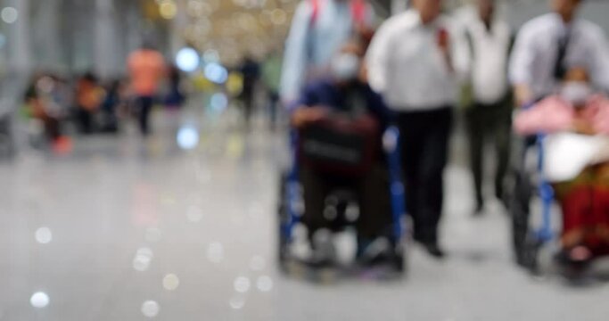 Blurred scene in modern airport terminal, featuring two elderly individuals in wheelchairs being assisted by airport personnel, with few accompanying people. Defocused picture for commercial use